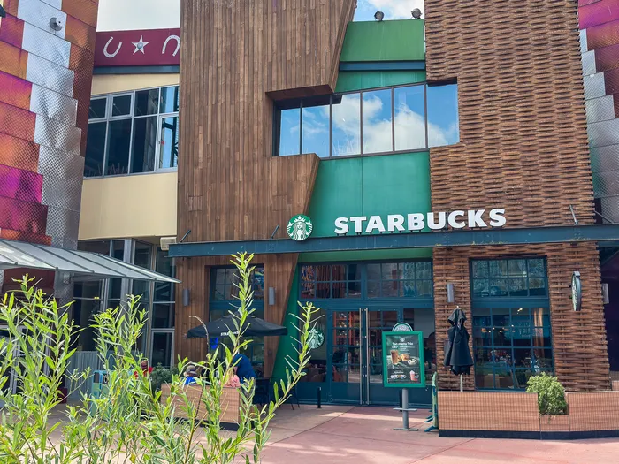 Façade en bois et vert du Starbucks du Disney Village, enseigne au logo, plantes et terrasse au premier plan.