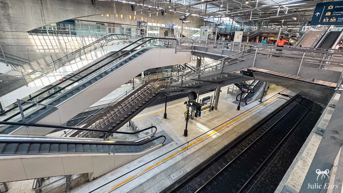 Quai de la gare TGV de Disneyland Paris vu d’en haut, avec les escalators qui descendent vers les voies encore vides.