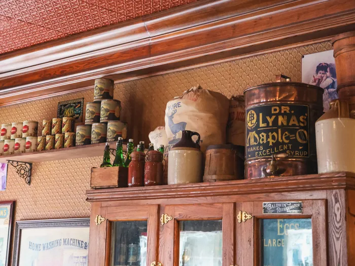 Étagère au décor rétro du Market House Deli avec boîtes anciennes, cruches et distributeur de sirop d’érable