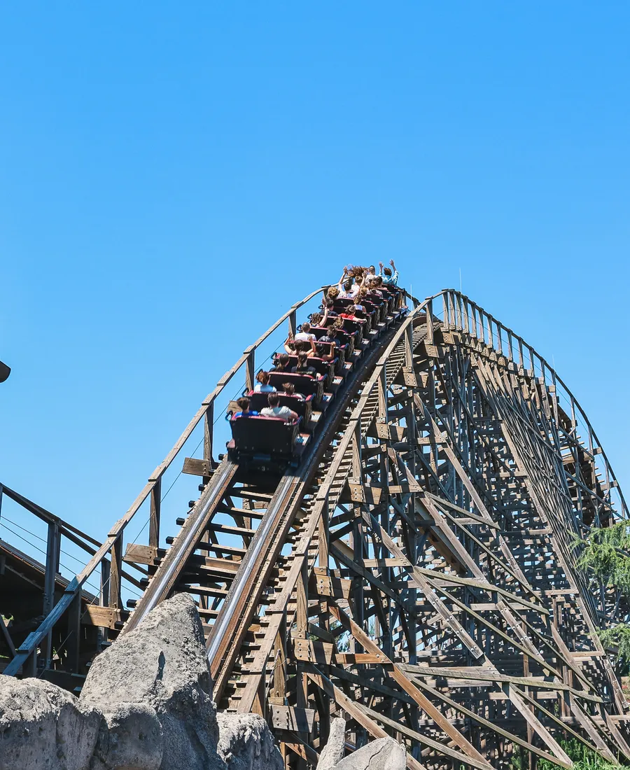 Train bondé du grand huit en bois Wodan dévalant sa structure sous un ciel bleu à Europa-Park