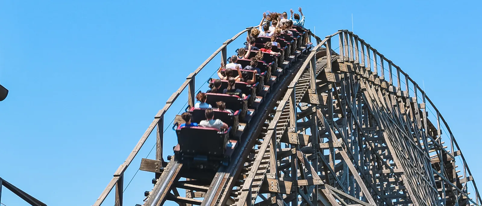 Train bondé du grand huit en bois Wodan dévalant sa structure sous un ciel bleu à Europa-Park