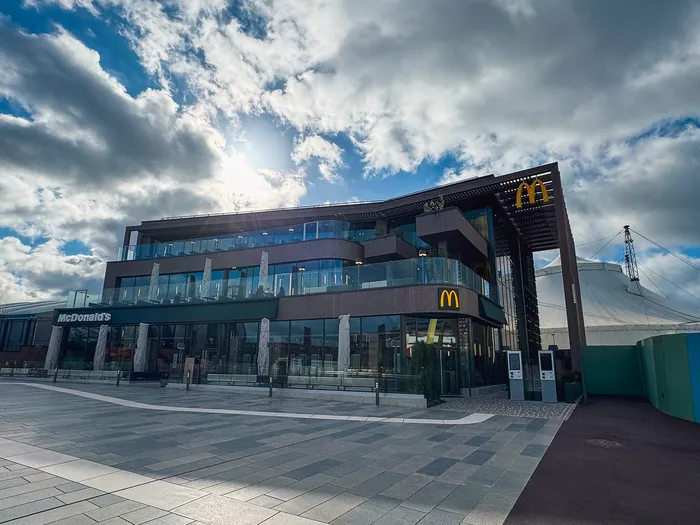 Grand bâtiment moderne vitré du McDon’s du Disney Village sous un ciel nuageux, enseigne dorée sur la façade.