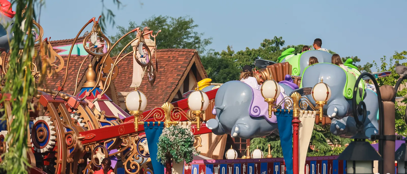 Éléphants Dumbo colorés tournoyant en l'air au-dessus des visiteurs, à Fantasyland, sous un ciel de fin d'après-midi.