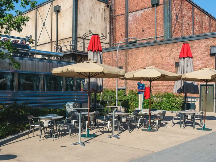 Terrasse du Super Diner avec parasols beiges et tables métalliques devant un bâtiment en brique du parc