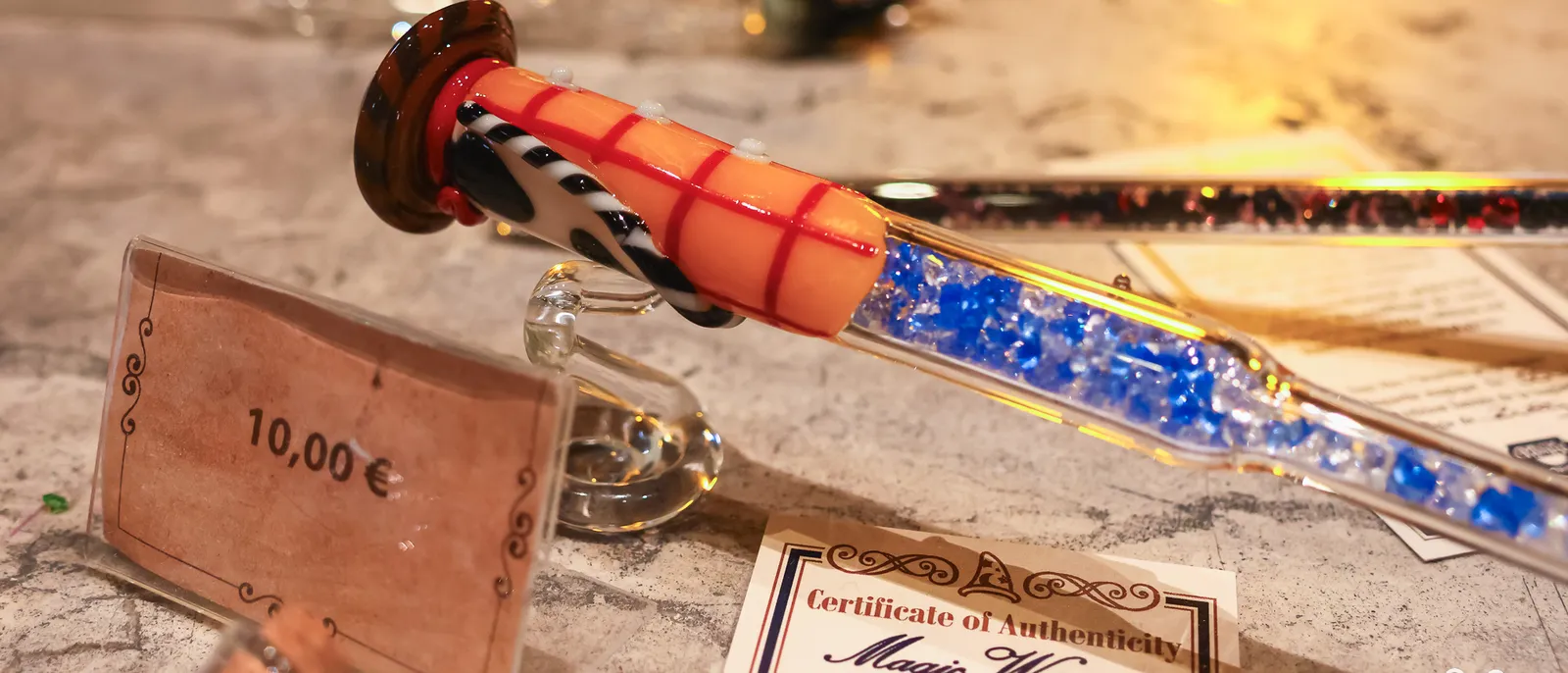Baguette magique en verre soufflé à 10€, étiquette de prix et certificat d’authenticité Magic Wand posés à côté.