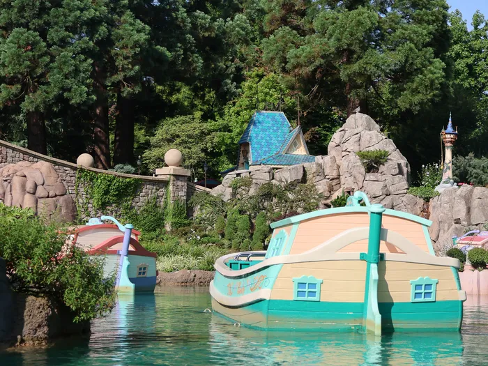 Bateau de la balade voguant sur les canaux turquoise du Pays des Contes de Fées, décors miniatures et tour de Raiponce en fond