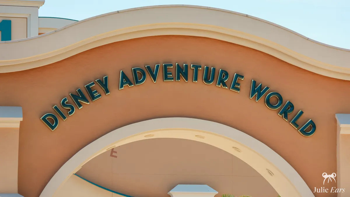 Disney Adventure World entrance arch at Disneyland Paris, its name in large dark green, gold-edged letters on a salmon facade, under a blue sky