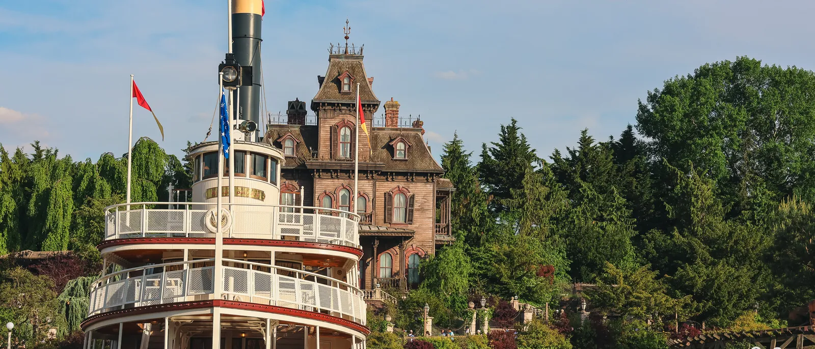 Le manoir victorien de Phantom Manor domine la rivière de Frontierland, un bateau à aubes blanc amarré au premier plan.