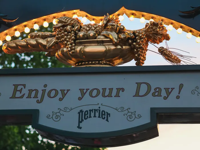 Enseigne dorée « Enjoy your Day ! » ornée de grappes et de blé, à l’entrée du Plaza Gardens sur Main Street.