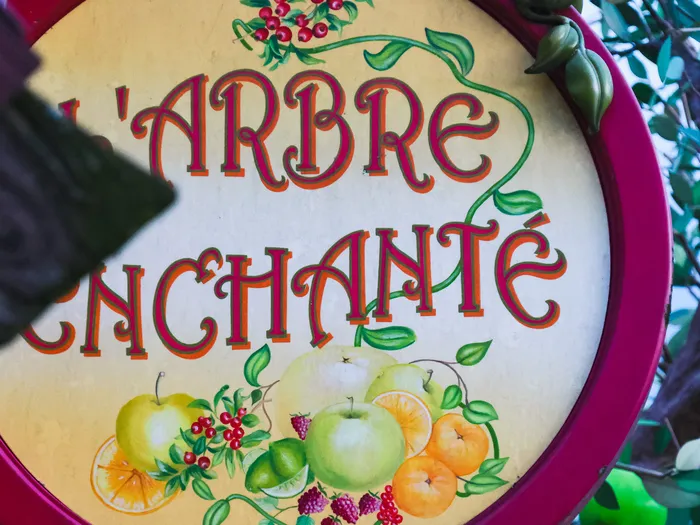 Enseigne ronde « L’Arbre Enchanté » ornée de pommes et d’oranges peintes, dans un cadre rose à Disneyland Paris.