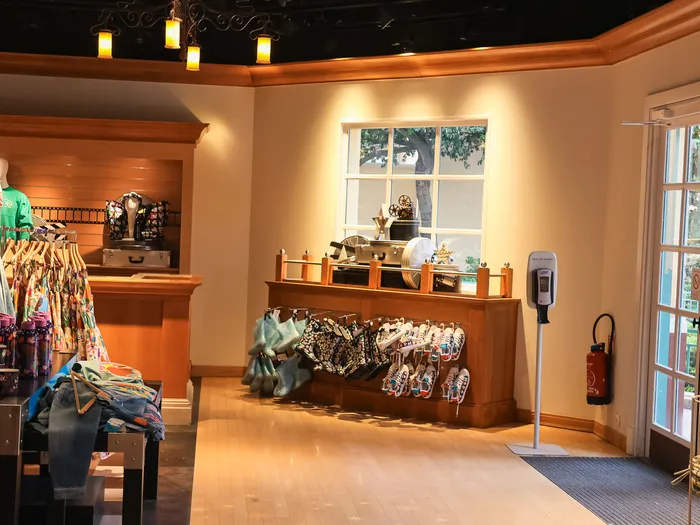 Intérieur du Walt Disney Studios Store avec mannequins habillés, comptoir en bois et portes vitrées