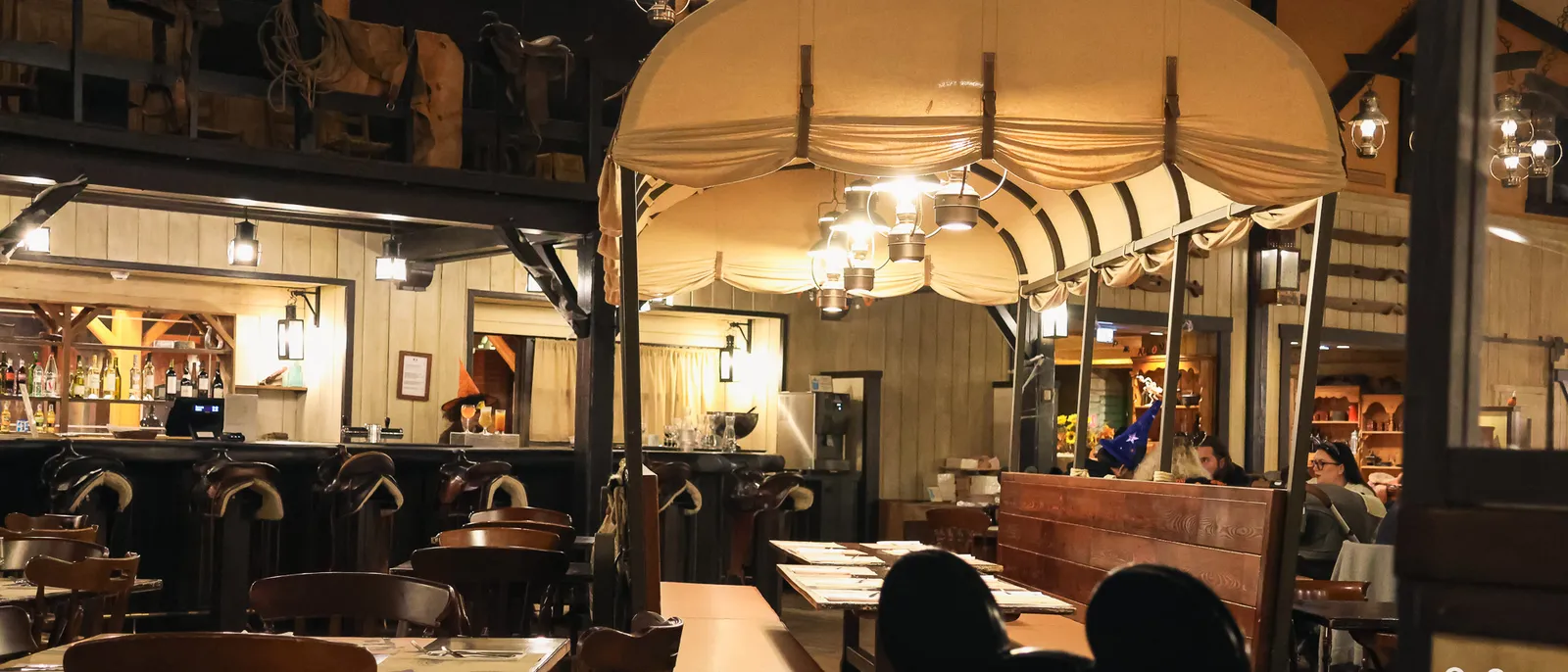 Salle de restaurant western d’un hôtel Disneyland Paris, chariot bâché éclairé de lanternes et tables en bois