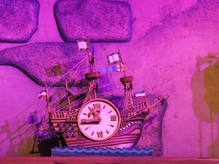 Horloge murale en forme de galion à pavillons colorés dans un décor rose de l’attraction Pinocchio à Fantasyland