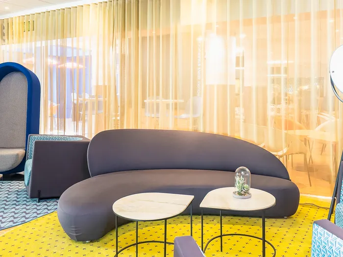 Salon commun de l'Adagio Aparthotel avec canapé courbe gris et tapis jaune près de Disneyland