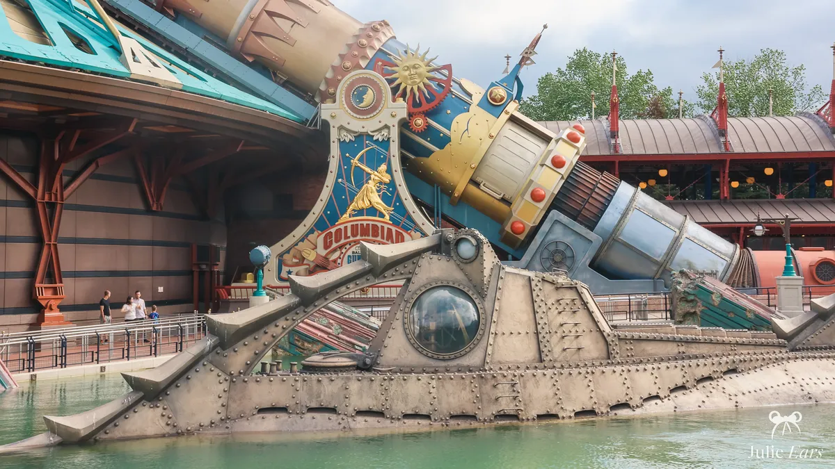 Base of the Space Mountain Columbiad cannon with its golden crest and sun, and the Nautilus submarine in the Discoveryland lagoon