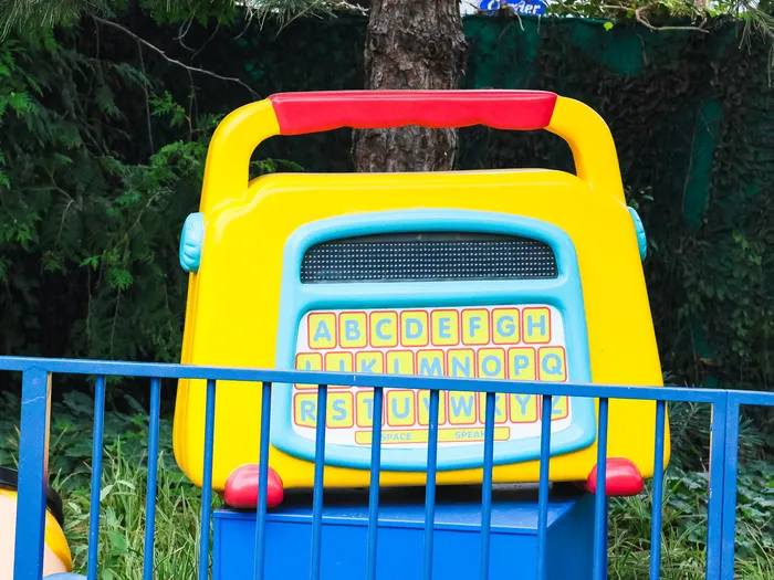 Jouet d’éveil géant jaune et bleu à clavier alphabétique, posé derrière une barrière bleue, à Worlds of Pixar