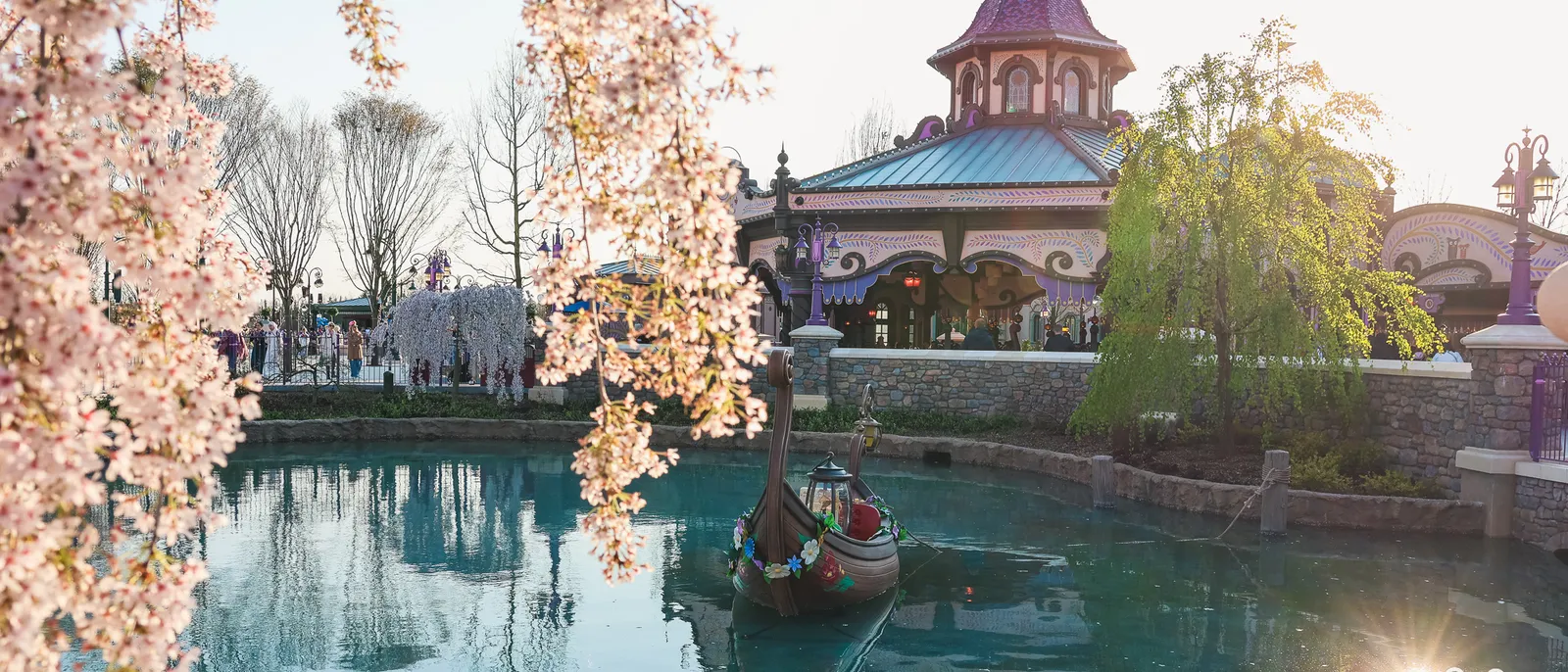 Barque décorée sur le lagon devant le pavillon de Raiponce Tangled Spin, cerisiers en fleurs au Parc Disney Adventure World.
