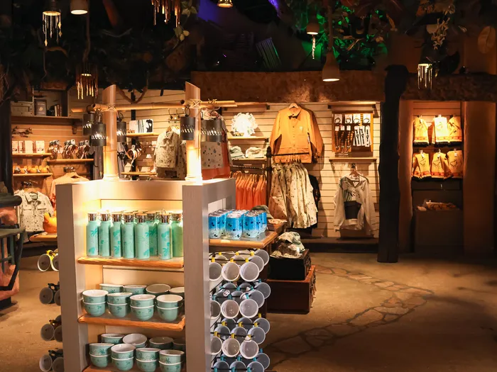 Inside the La Girafe Curieuse shop at Disneyland Paris, with a wooden stand full of turquoise ceramic mugs and cups and clothes hanging on the wall.