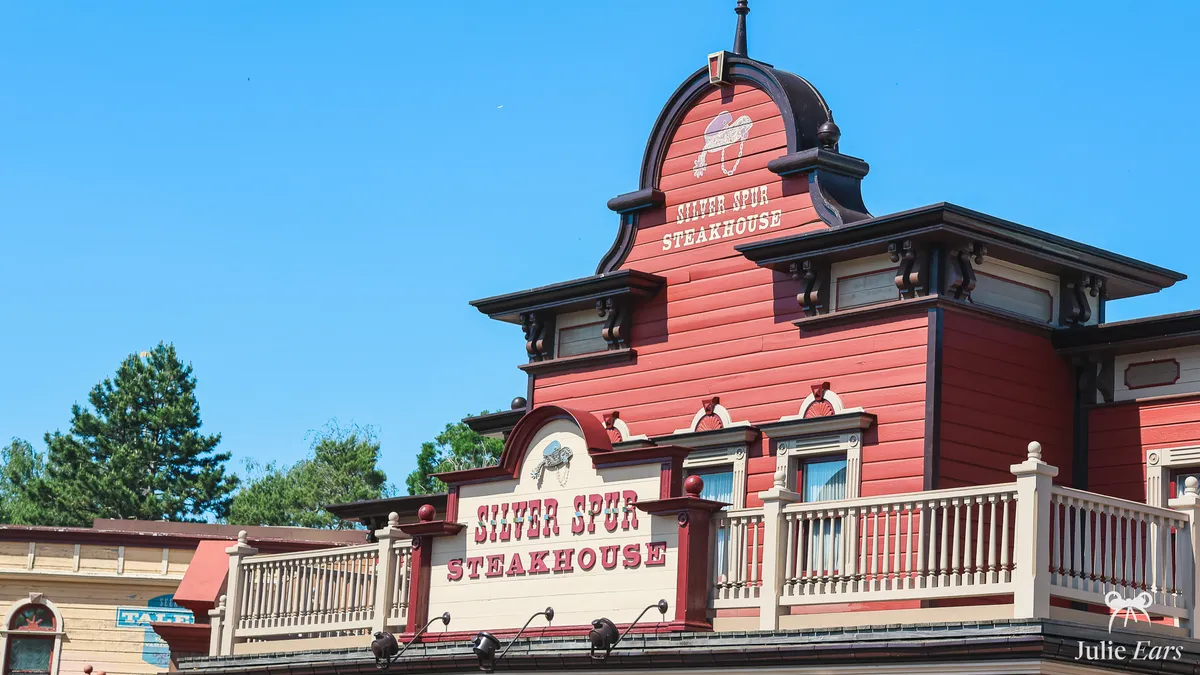 Red wooden facade of the Silver Spur Steakhouse in Frontierland at Disneyland Paris, with its sign on the pediment and another on the balcony