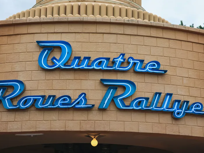 Enseigne au néon bleu « Quatre Roues Rallye » sur la façade en brique claire de l’attraction Cars.