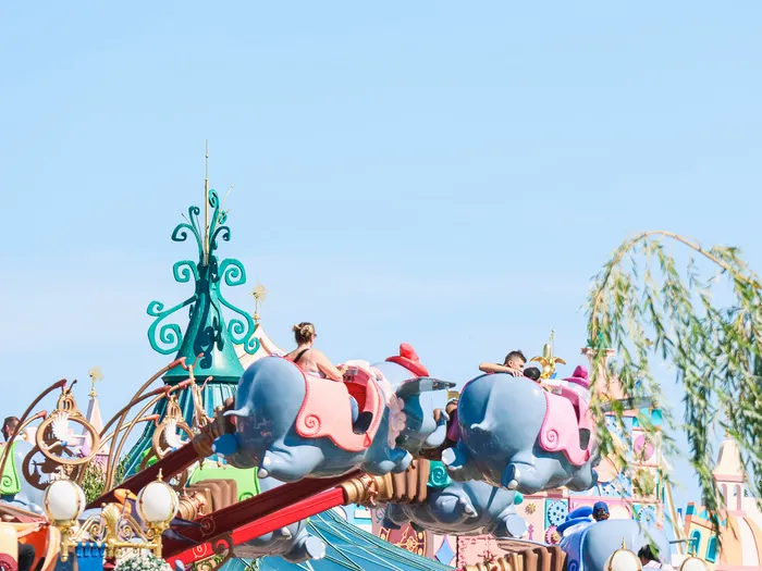 Nacelles éléphants du manège Dumbo en vol contre un ciel bleu, avec des visiteurs à bord à Fantasyland