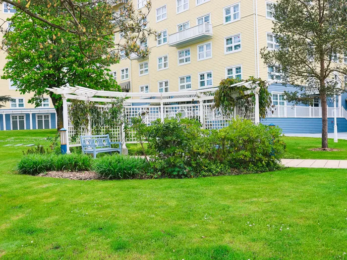 Jardin engazonné avec banc et pergola fleurie devant la façade du Newport Bay Club.