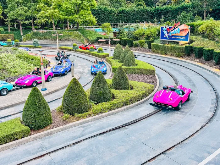 Voitures colorées circulant sur les pistes bordées de topiaires de l’attraction Autopia à Discoveryland.