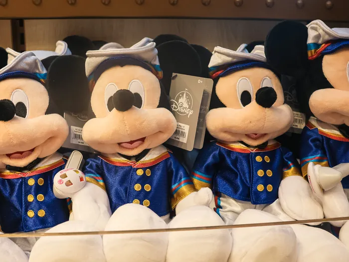 Four Mickey soft toys in navy sailor outfits with gold buttons, lined up on a shelf.