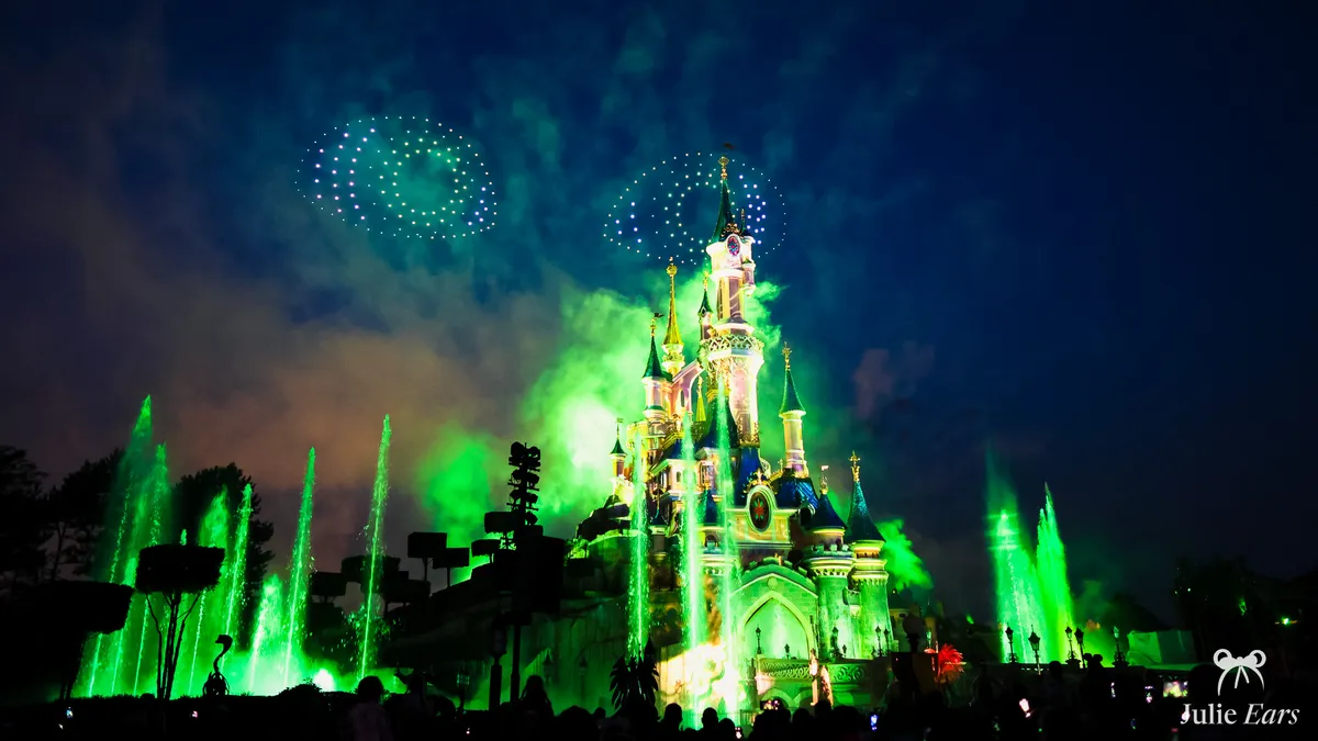 Disney Tales of Magic night-time show at Disneyland Paris: Sleeping Beauty Castle lit in green, with green fountains and drones forming circles