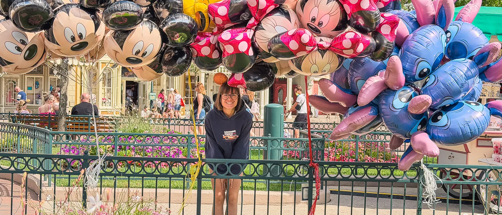 Grappes de ballons Mickey, Minnie et Stitch tenues devant Main Street à Disneyland Paris, fleurs au premier plan.