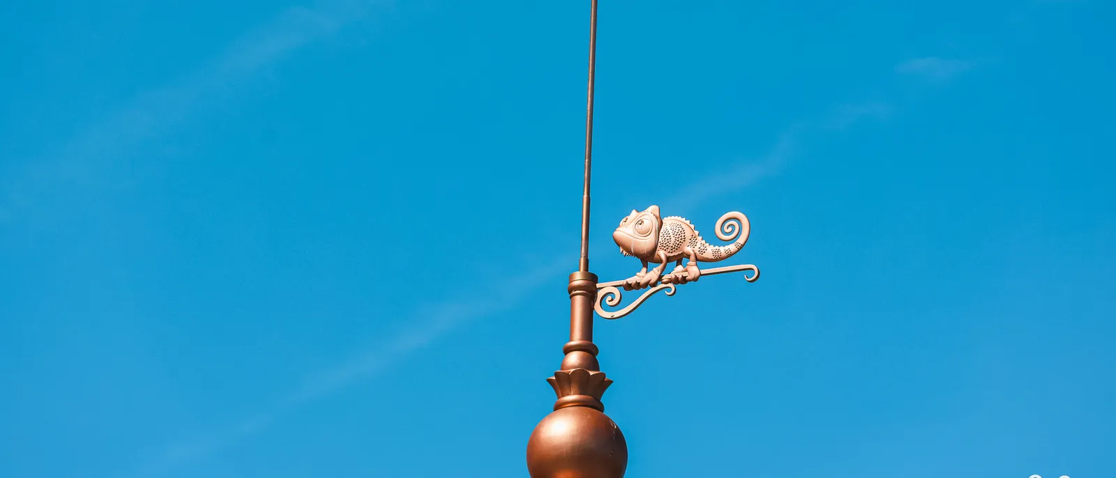 Girouette en cuivre ornée du caméléon Pascal de Raiponce, sur fond de ciel bleu à Disneyland Paris.