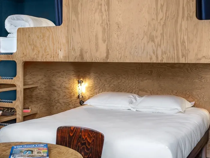 Family room at the Eklo hotel with a double bed, light wood bunk beds and a table area.