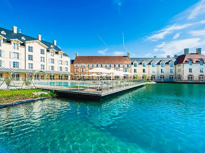 Façade classique d’un hôtel au bord du lac avec piscine couverte reliée par une passerelle, près de Disneyland Paris.