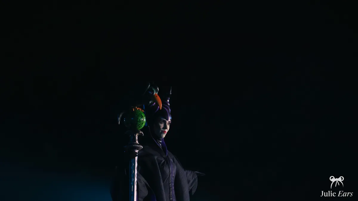 Maleficent, with her horns and green orb sceptre, standing out in the half-light during a show at Disneyland Paris.