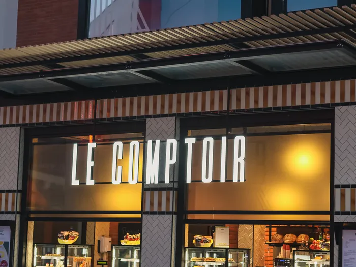 Façade vitrée éclairée du Comptoir, enseigne blanche et vitrines de sandwichs et pâtisseries au Disney Village.
