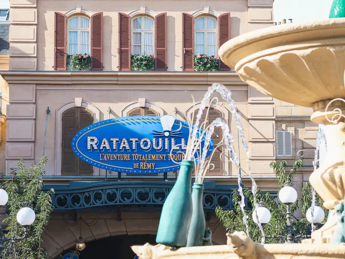 Bottle fountain of La Place de Rémy and the blue Ratatouille ride sign, before a Haussmann-style frontage with window boxes, Disneyland Paris