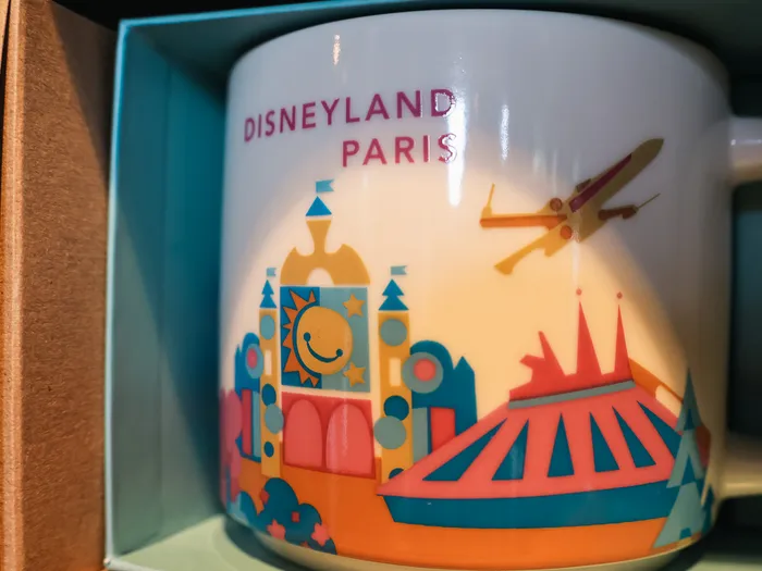 Close-up of a You Are Here Collection Disneyland Paris mug from Starbucks: the carousel, Space Mountain and Star Tours drawn in bright colours