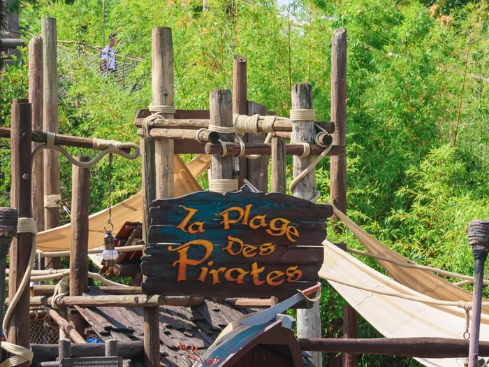 Panneau de bois gravé « La Plage des Pirates » au milieu de la structure de jeux, devant les bambous