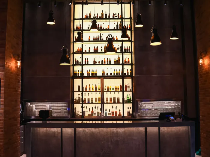 Comptoir du bar du Bleecker Street Lounge à l’Hôtel New York, avec un haut mur de bouteilles rétroéclairé.