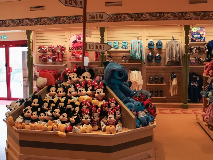 Large bin of Mickey, Minnie and Stitch soft toys in front of signposts and a red door