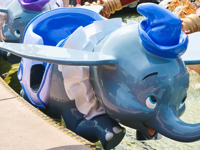 Nacelle en forme d’éléphant Dumbo bleu coiffé de son chapeau, à l’arrêt au-dessus du bassin à Fantasyland