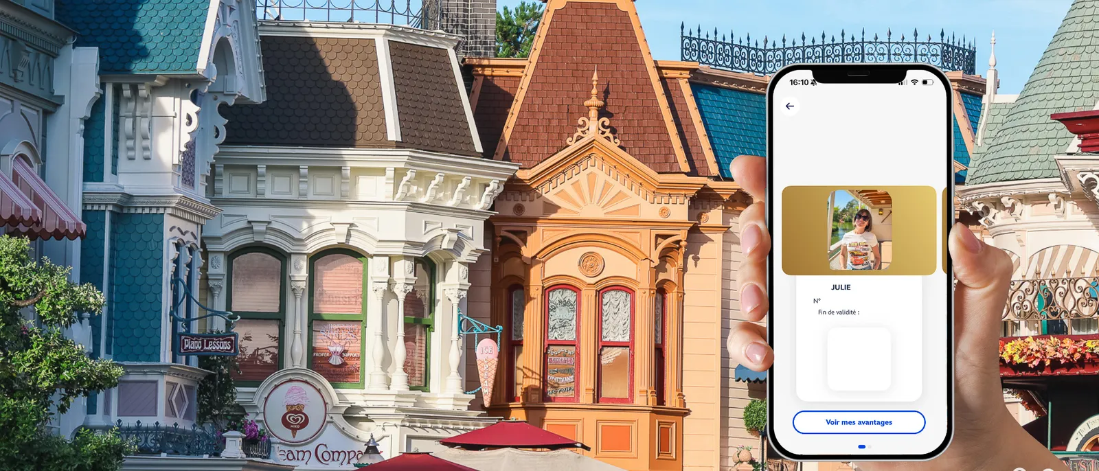 Main tenant un smartphone affichant la carte de membre Disneyland Pass, devant les façades de Main Street USA.