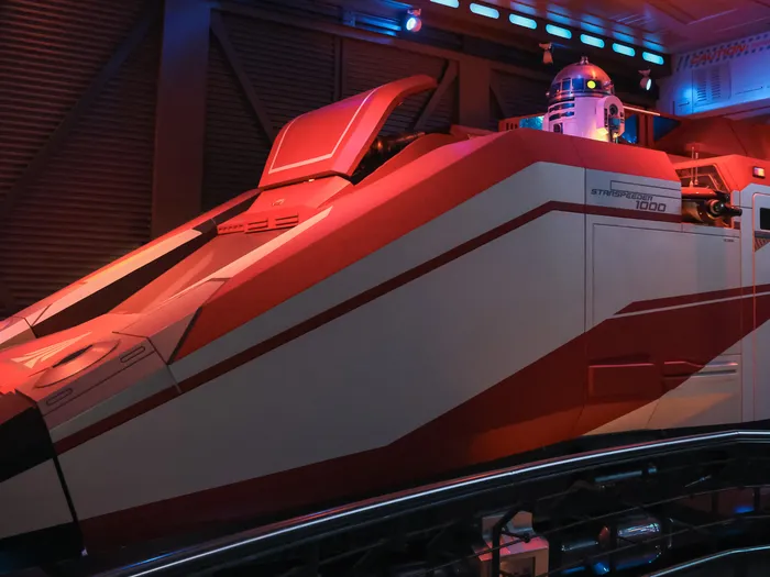 Navette Starspeeder 1000 rouge et blanche surmontée d'un droïde R2, sous un éclairage rouge dans Star Tours à Discoveryland