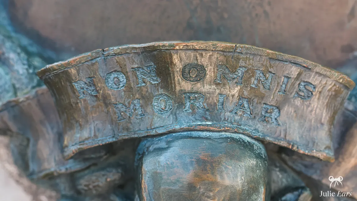 Close-up of the Latin motto "Non Omnis Moriar" in relief on a weathered metal band at the entrance to Phantom Manor, Frontierland, Disneyland Park