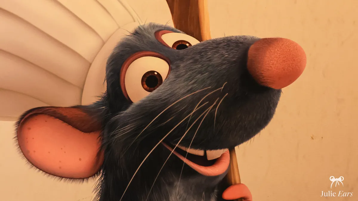 Close-up of Remy, the chef rat from Ratatouille, smiling under his white chef’s hat, in the Bistrot Chez Rémy setting at Disney Adventure World