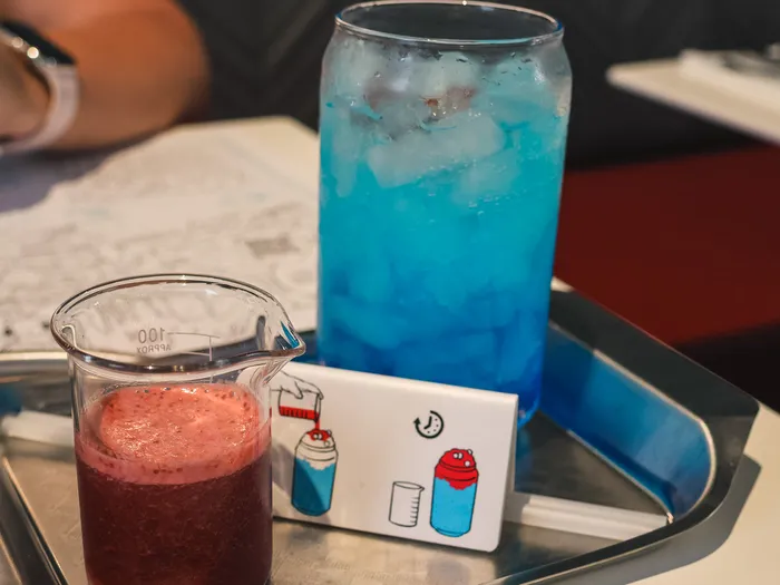 Boisson bleue et smoothie rouge servis dans un bécher sur un plateau métallique au restaurant PYM Kitchen.