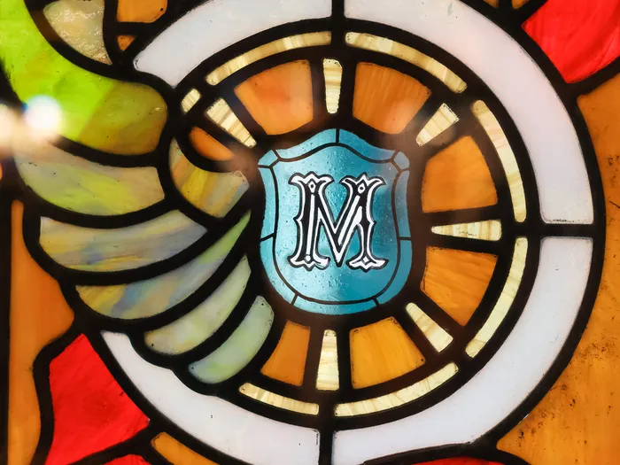 Close-up of the Main Street Motors stained glass: white wheel, blue crest with an "M" monogram and red ribbons, at Disneyland Paris.