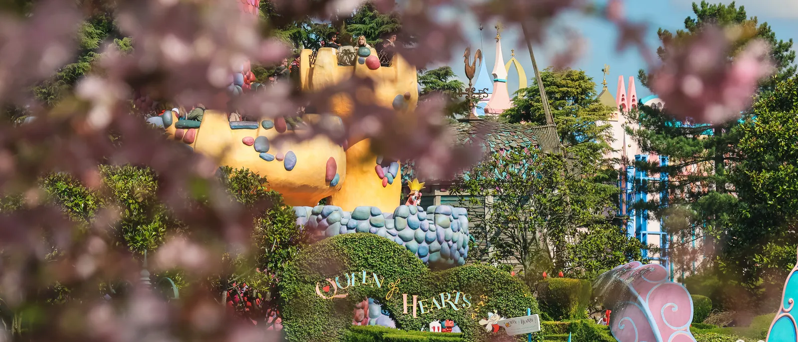 Enseigne Queen of Hearts du labyrinthe d’Alice, vue au printemps derrière des cerisiers en fleurs, à Fantasyland.