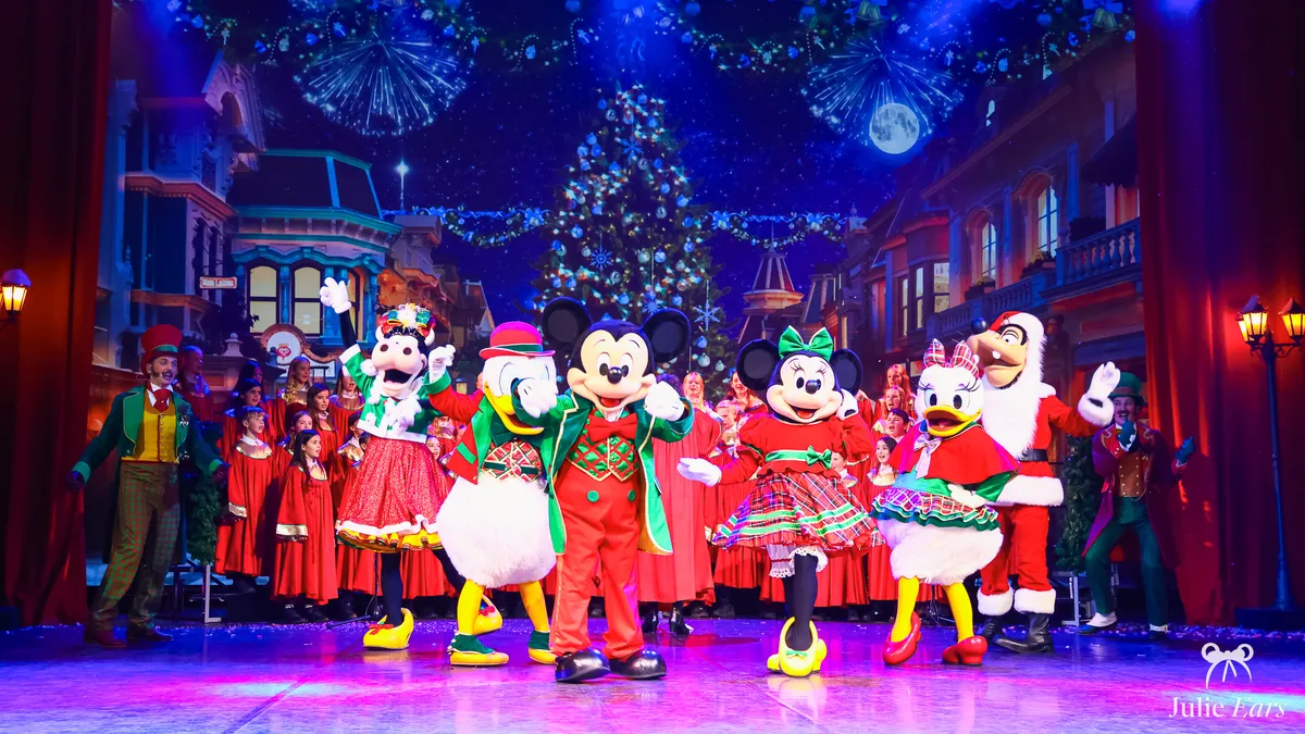Mickey, Minnie, Donald, Daisy et Dingo en tenue de fête sur scène avec une chorale pendant le spectacle Chantons Noël à Disneyland Paris