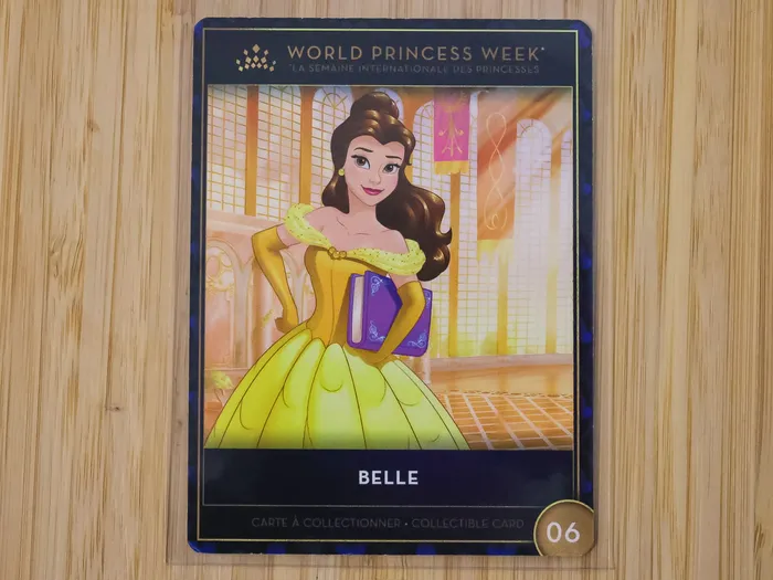 Carte à collectionner World Princess Week montrant la princesse Belle en robe jaune tenant un livre dans un décor de château.